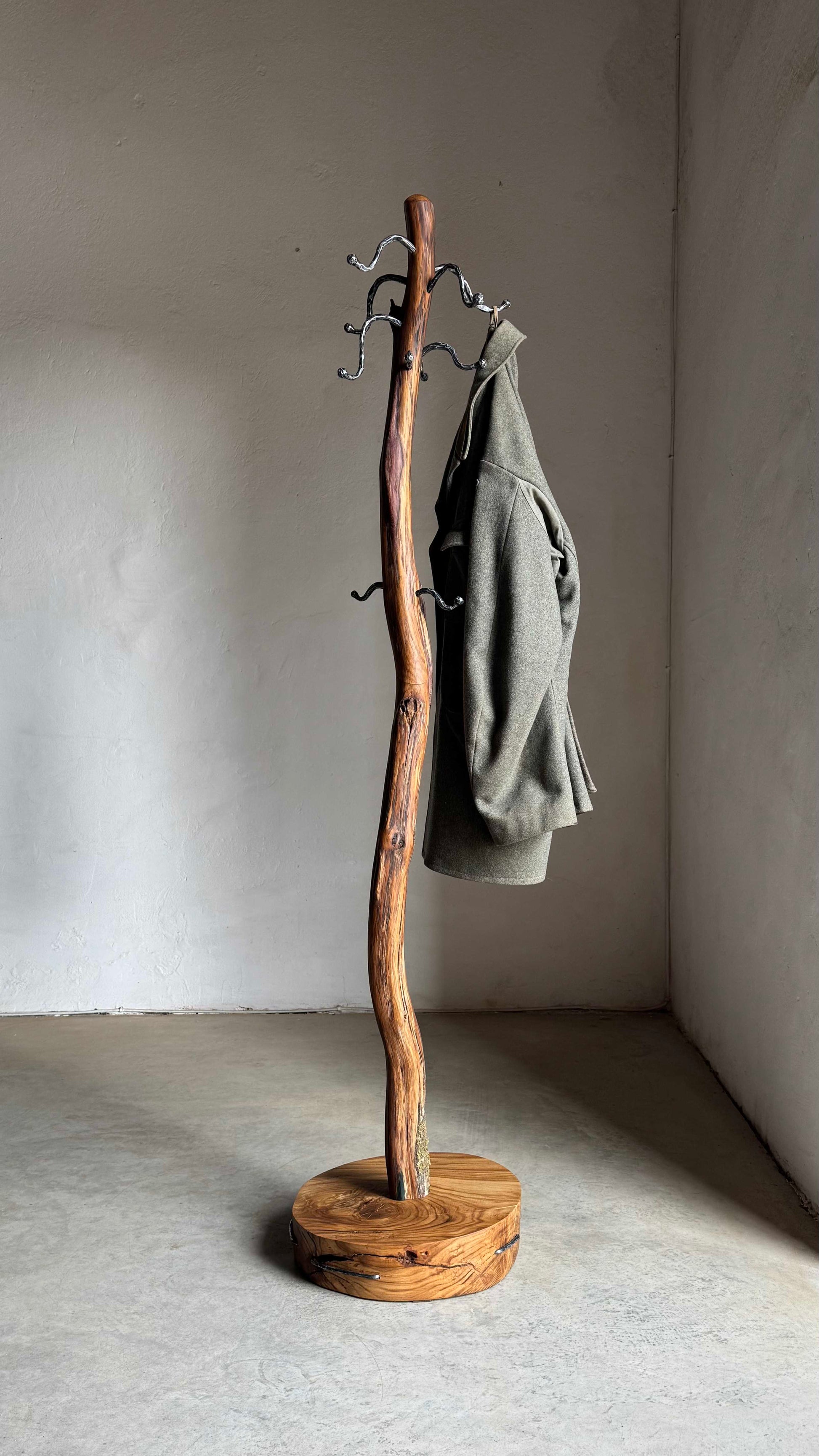 Oak Coat Rack with steel hangers Wooden coat stand with a coat on it against a plain wall.